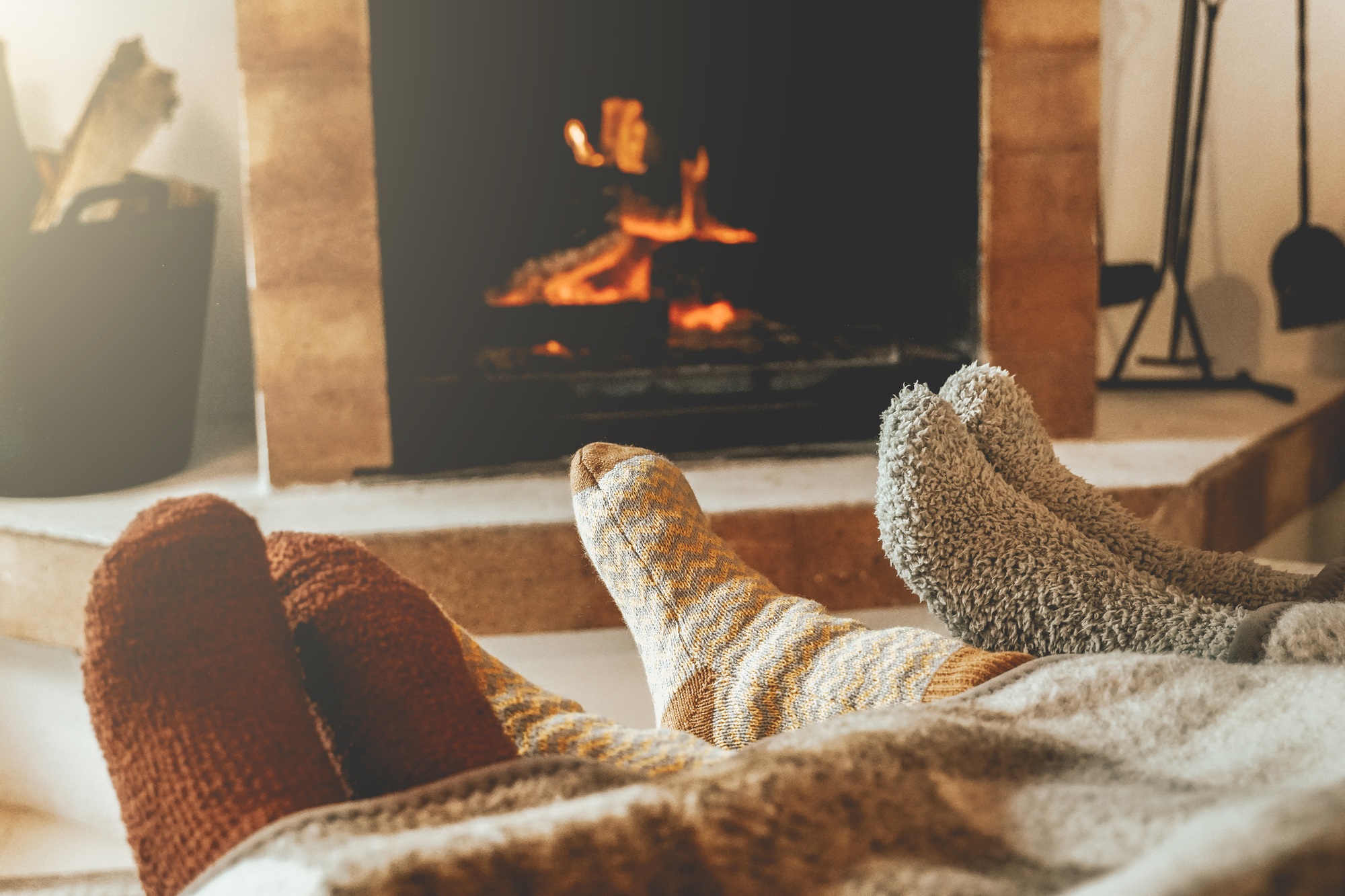 Family resting feet by fireplace. People warming feet with blanket and socks by cozy fire.